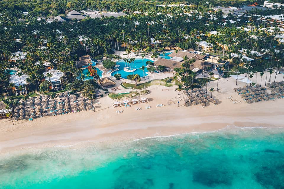 Aerial resort view with blue pools, beach access, and palm-lined grounds