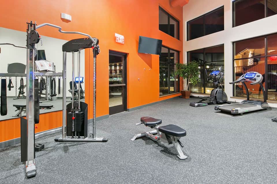 Modern fitness center with orange accent walls, treadmills, weight equipment, and mirrors