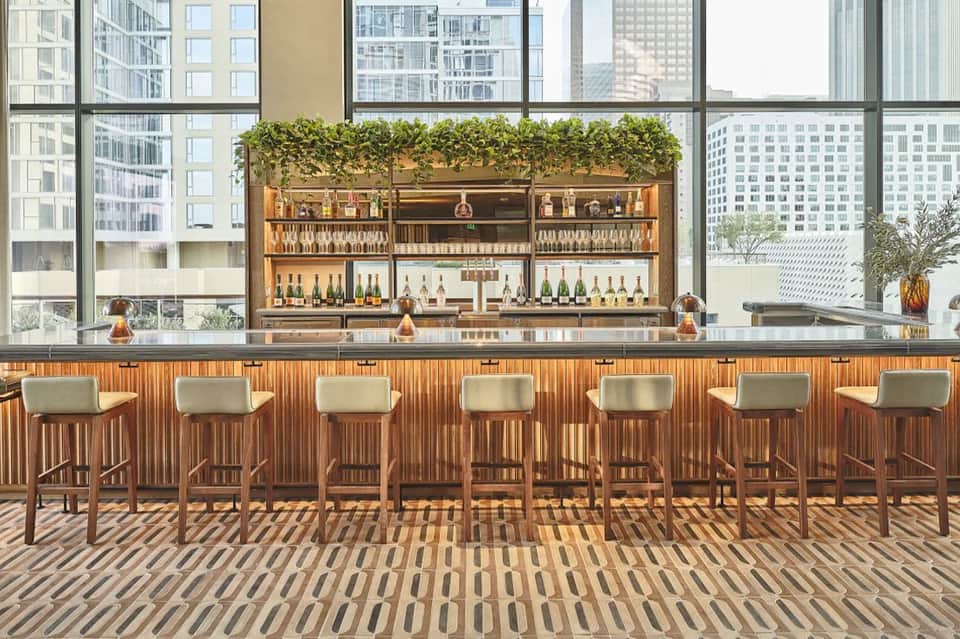 Modern rooftop bar with wooden stools, extensive liquor selection, and city skyline views