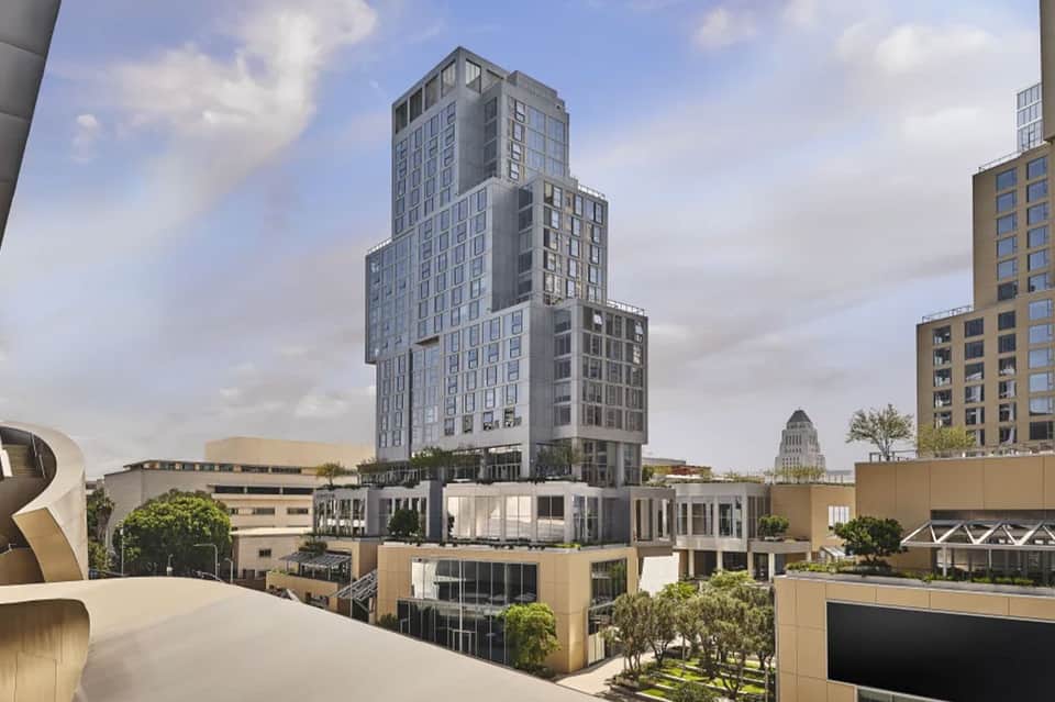 Modern mixed-use building with stepped architecture and landscaped rooftop among downtown buildings