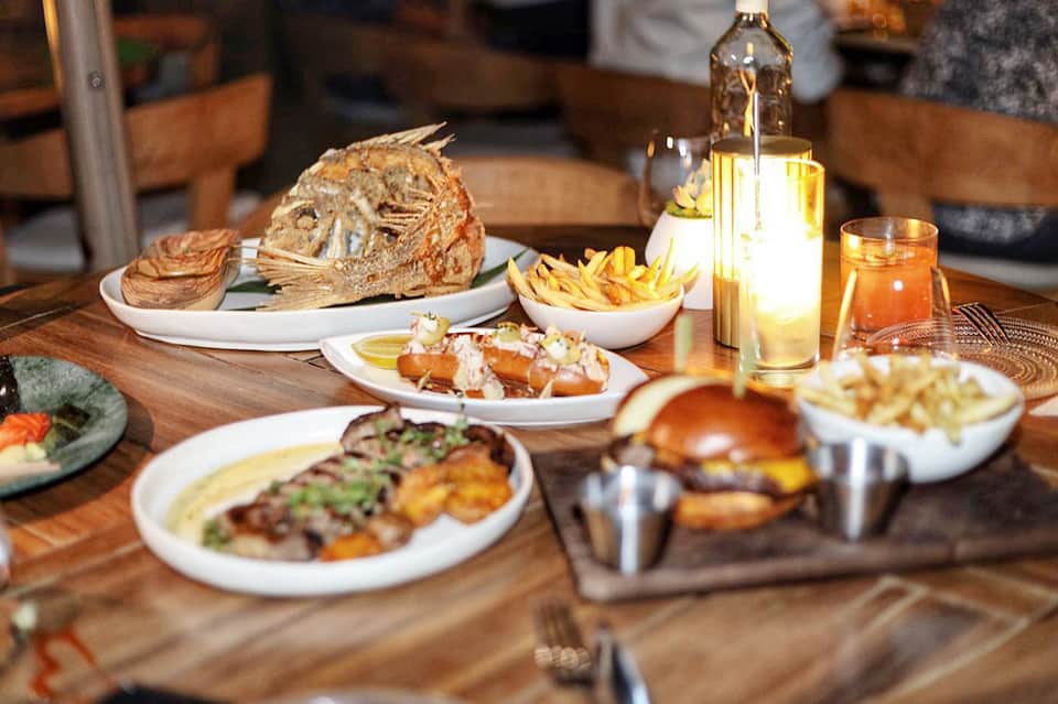 Fine dining table with grilled fish, bread, fries, and wine bottle in warm restaurant lighting