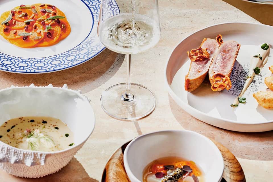 Fine dining table with gourmet dishes, blue and white plates, seafood appetizers, and wine glass