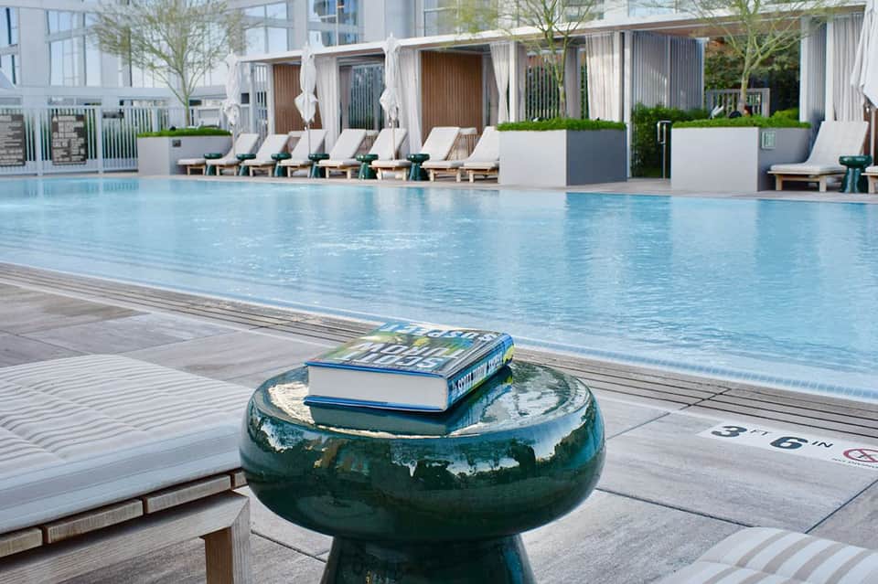 Modern resort pool with white lounge chairs, contemporary shade structures, and high-rise building