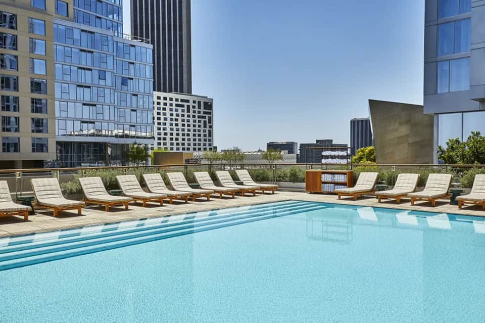 Urban rooftop pool with lounge chairs, city skyline views, and modern high-rise buildings in background