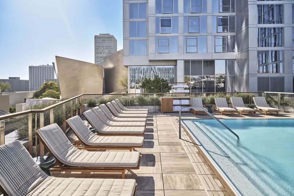 Resort rooftop pool with striped lounge chairs, city skyline, and modern architecture