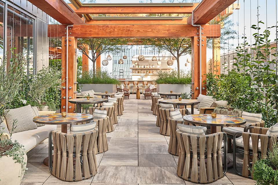 Upscale rooftop restaurant with wooden pergola, dining tables, greenery, and hanging pendant lights