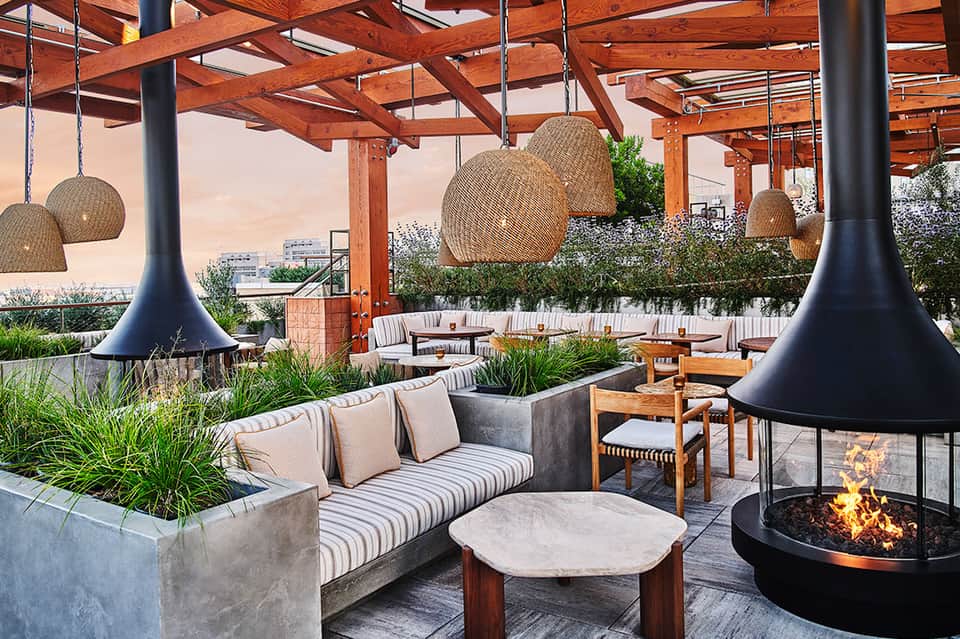 Modern rooftop lounge with wooden pergola, fire pits, woven pendant lights, and striped seating