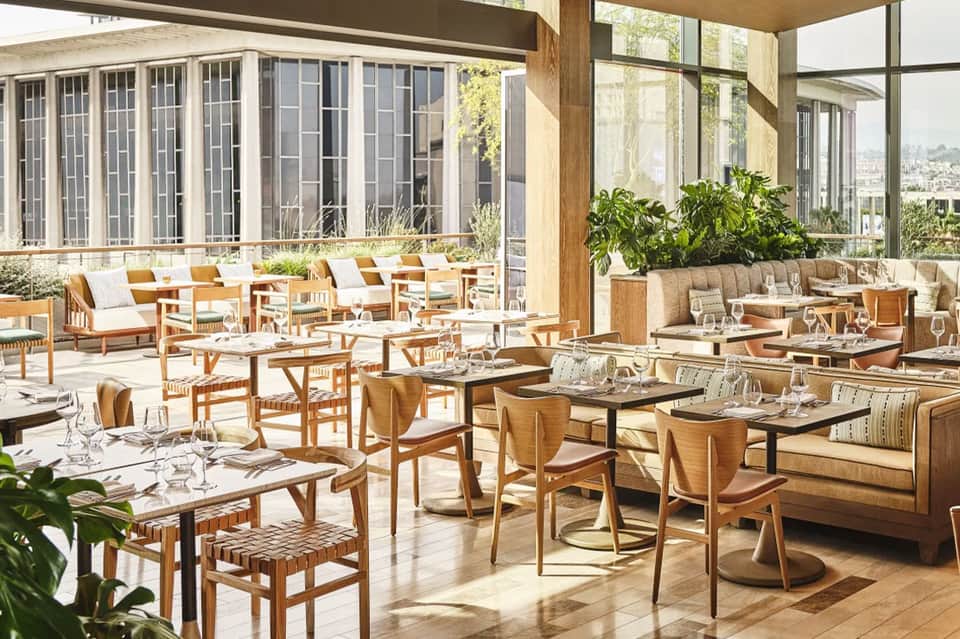 Upscale resort dining area with wooden furniture, floor-to-ceiling windows, and city skyline views