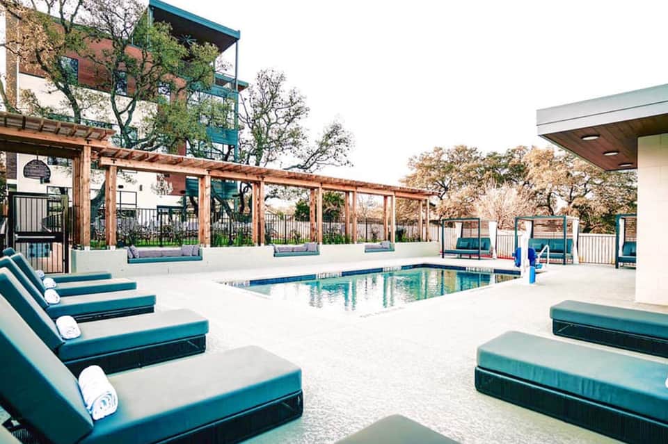 Resort pool with teal lounge chairs, wooden pergola, and landscaping