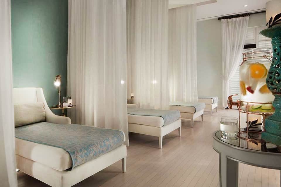 Spa relaxation room with lounge chairs, mint walls, white curtains, and flower display