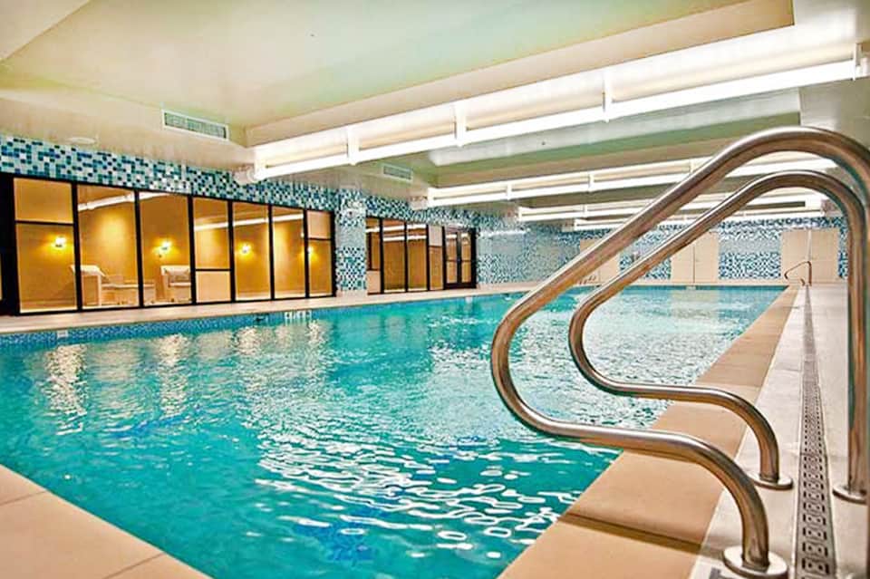 Indoor lap pool with turquoise water, tiled walls, and metal handrails