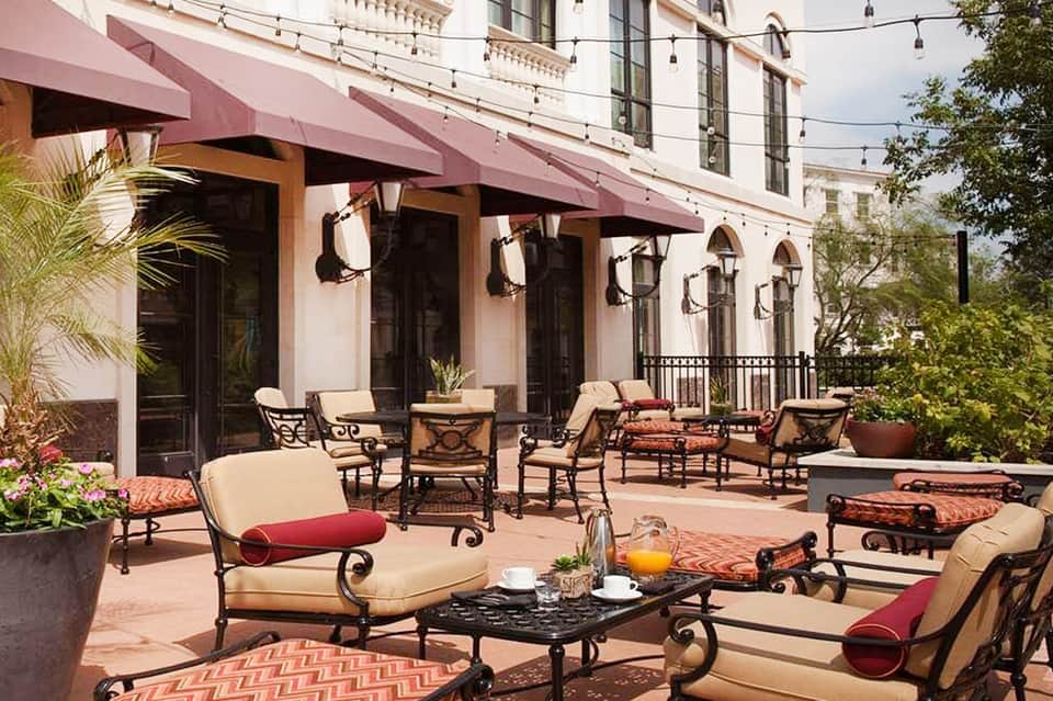 Elegant terrace seating area with beige cushioned chairs, red accents, and decorative plants near a building