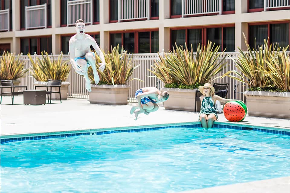 Children playing by pool with animated characters jumping and child in hat sitting poolside