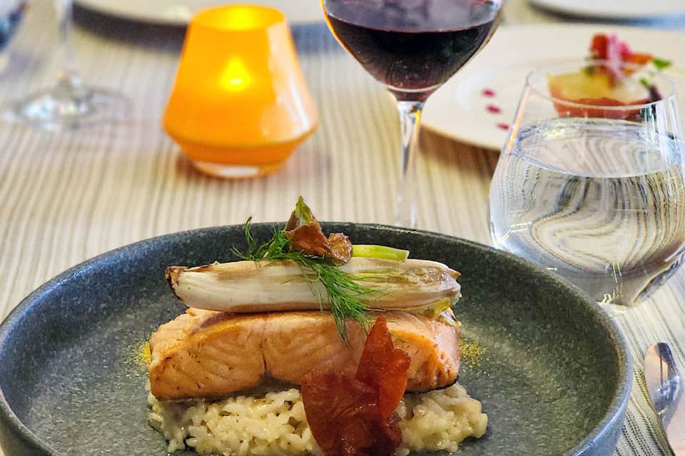 Fine dining plate of salmon with risotto, served with wine and cocktails on striped tablecloth