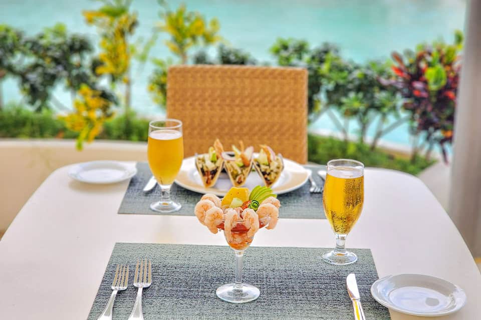 Outdoor dining table with appetizers, beer glasses, tacos, and ocean view background