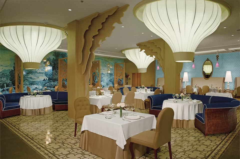Elegant dining room with shell-shaped light fixtures, gold columns, and round white-draped tables