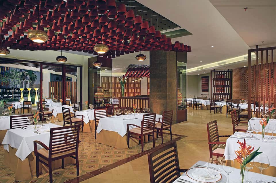 Elegant fine dining restaurant with red acoustic ceiling, white tablecloths, and tropical flowers