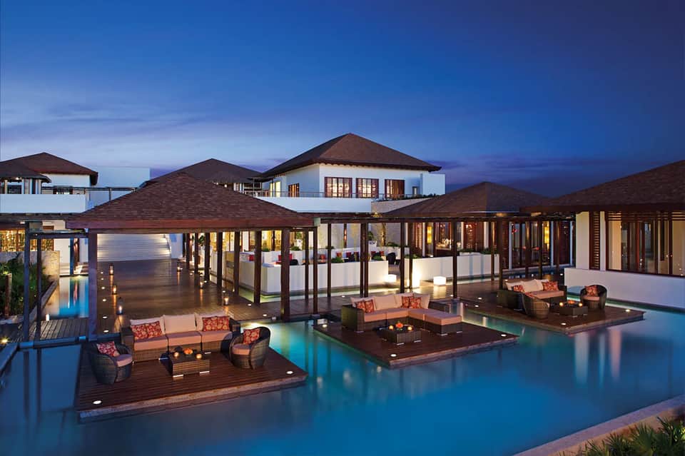 Luxury waterfront villa with modern architecture, illuminated at dusk, infinity pool