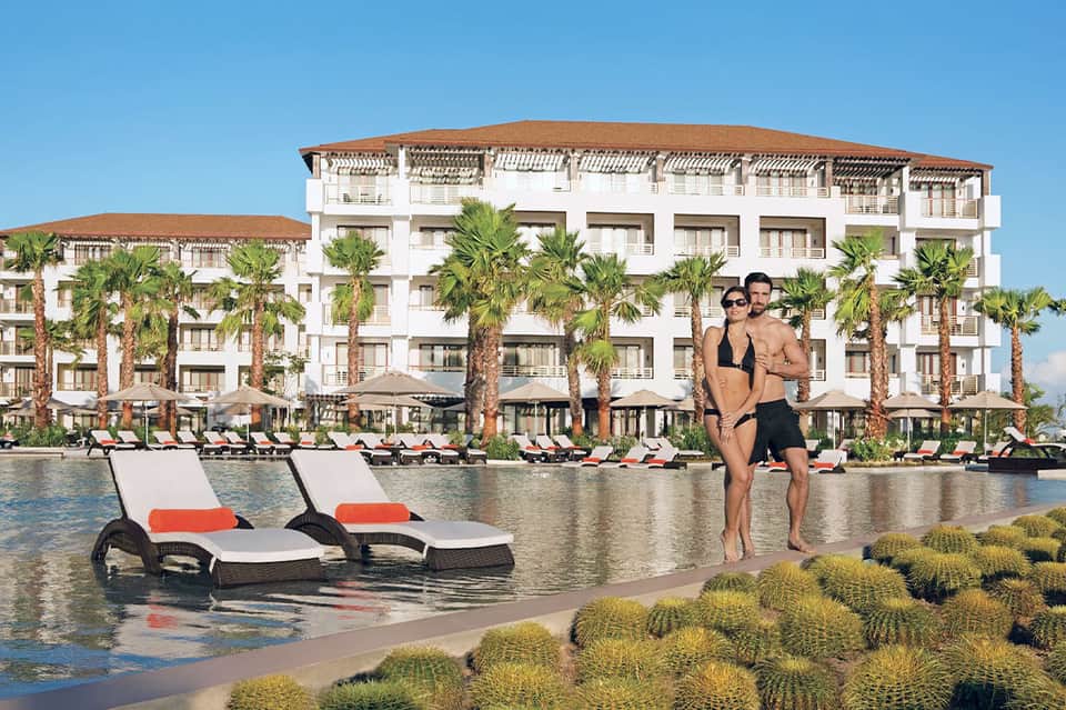 Couple at water's edge with luxury beachfront resort and palm trees in background