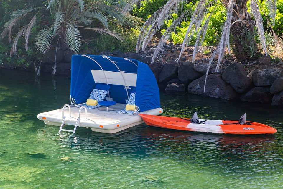 Floating blue cabana with kayak docked in turquoise lagoon surrounded by tropical palms