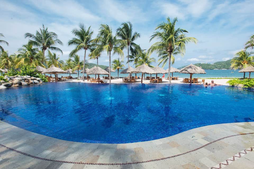 Beachfront infinity pool with thatched cabanas and ocean view