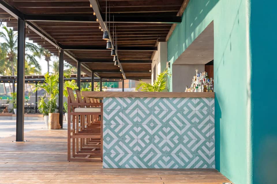 Beachfront bar with patterned tile counter and wooden seating under pergola