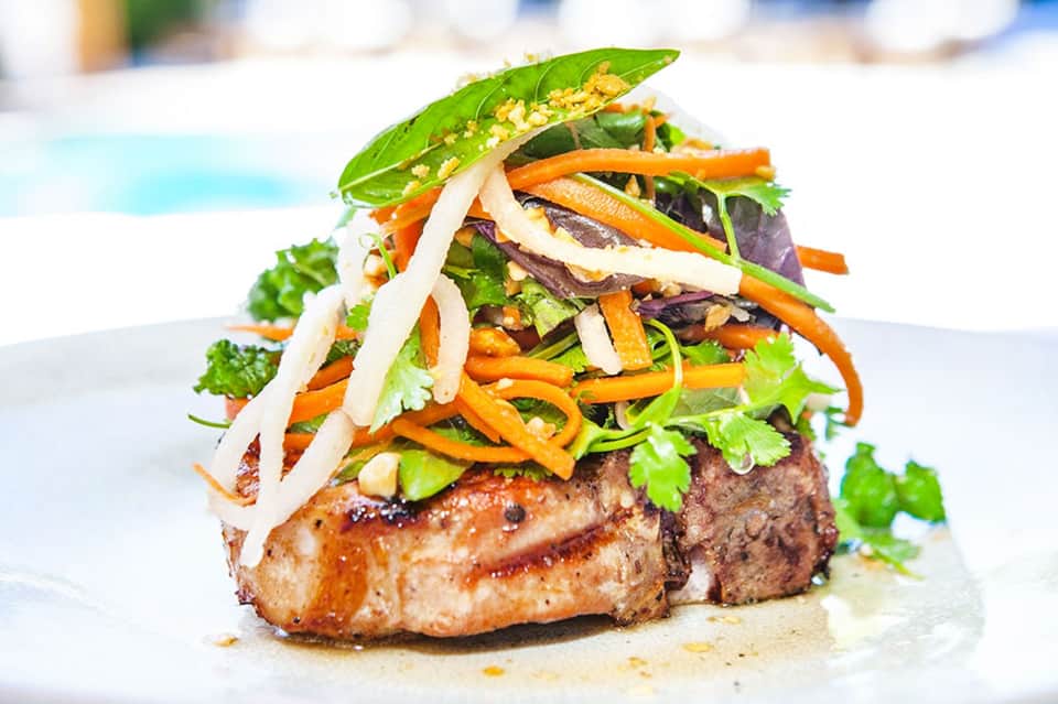 Gourmet plated meat dish with colorful vegetable garnish and fresh herbs