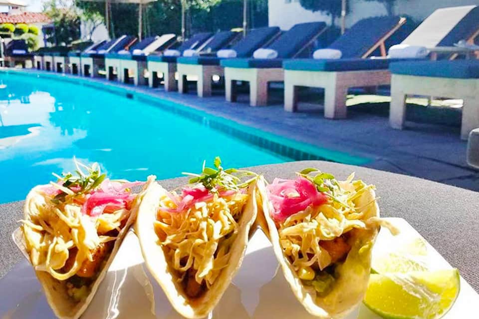 Three gourmet tacos with crispy shells and toppings poolside at a luxury resort