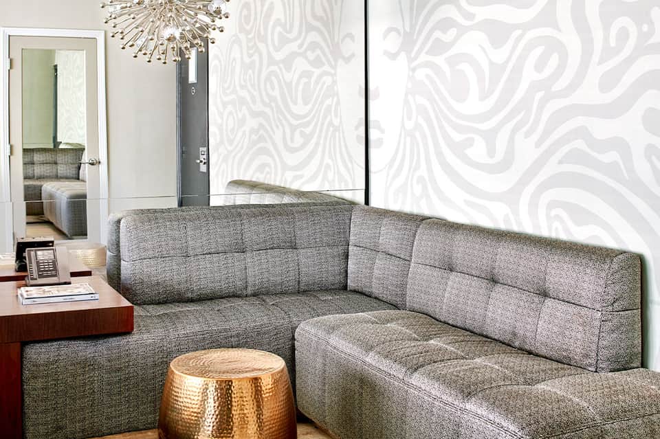 Modern living room with gray quilted sectional sofa, geometric wallpaper, and ceiling fixture