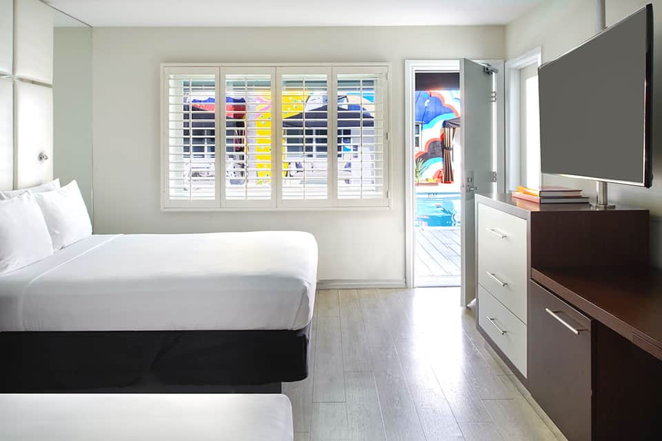 Beachfront hotel room with queen bed, white shutters, flat-screen TV, and ocean view balcony