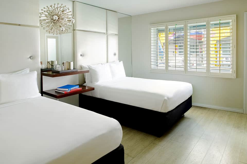 Clean hotel room with two beds, modern furniture, and colorful shutters on windows