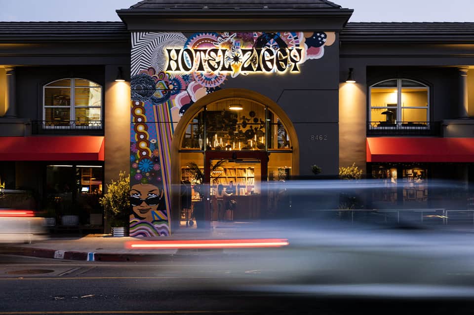 Hotel Ziggy storefront at night with colorful psychedelic mural and illuminated signage