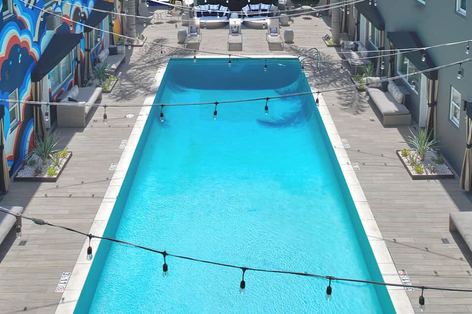 Lap pool viewed from above with bright blue water, wooden deck, lounge chairs, and colorful wall art