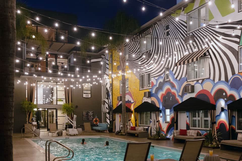 Vibrant nighttime courtyard pool with colorful murals, string lights, and lounge seating