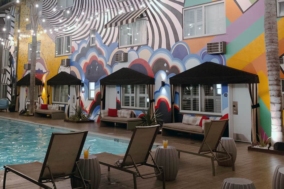 Indoor pool deck with colorful mural, black umbrellas, and lounge chairs