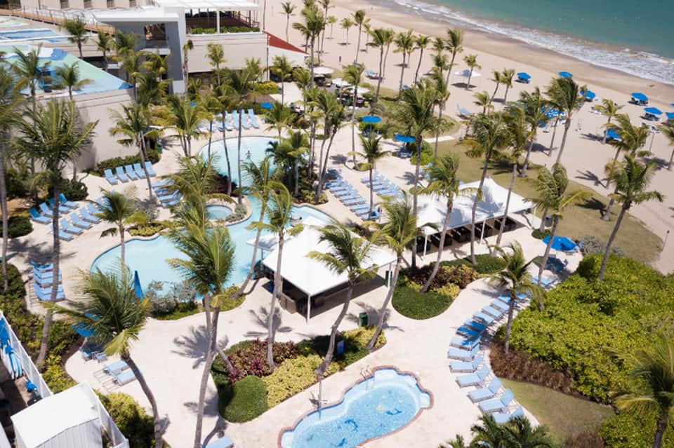 Aerial view of beachfront resort with multiple pools, palm trees, beach, and ocean