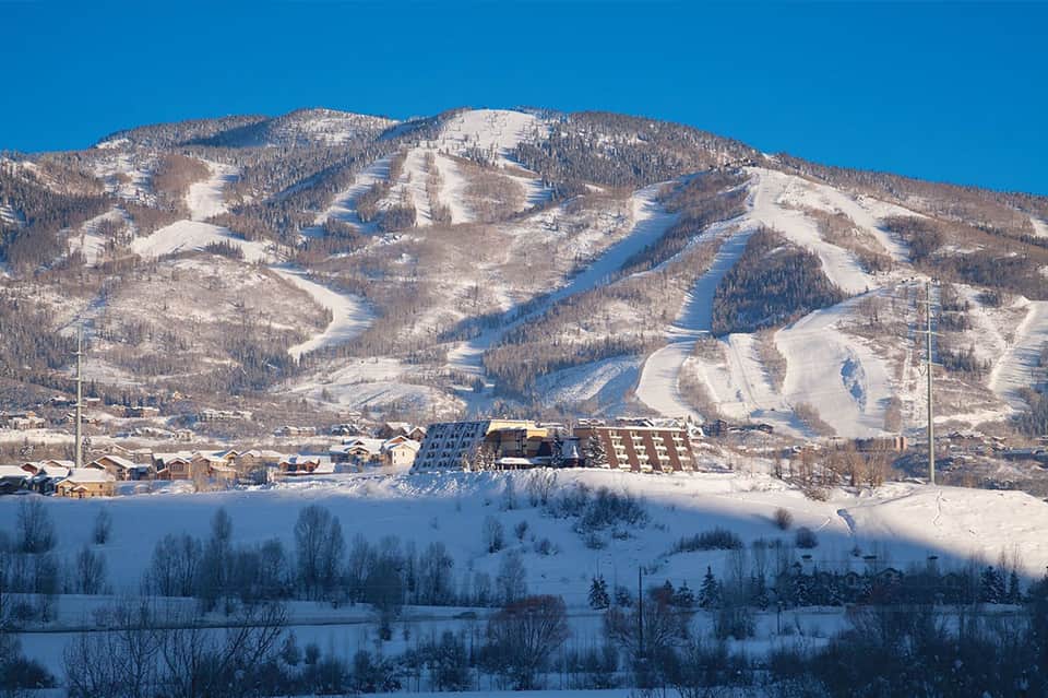 Snow-covered ski mountain with multiple runs and lodge building at base in winter
