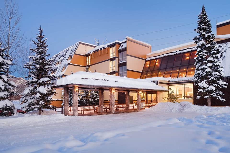 Snow-covered resort exterior with warm lighting, evergreen trees, and modern architecture