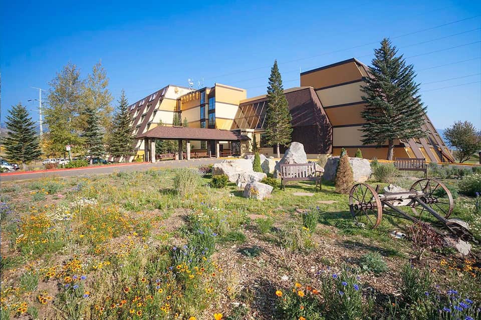 Modern hotel building with distinctive angular architecture surrounded by wildflowers and tall evergreen trees