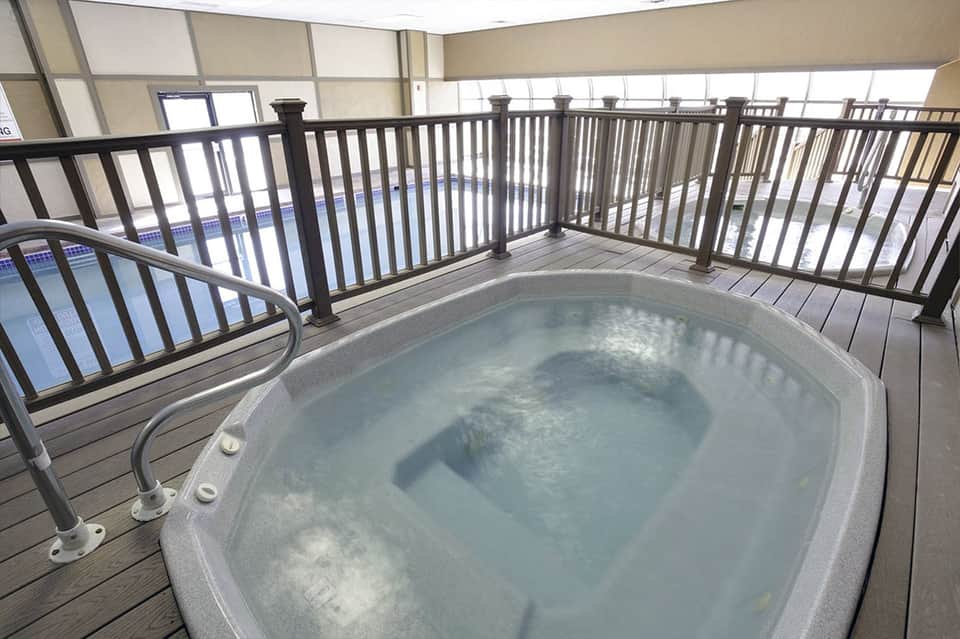 Hot tub on rooftop deck with metal railing overlooking indoor pool area