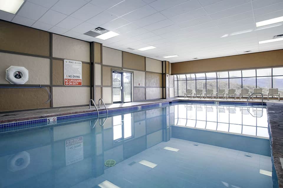 Indoor heated swimming pool with large windows, lounge chairs, and mountain views