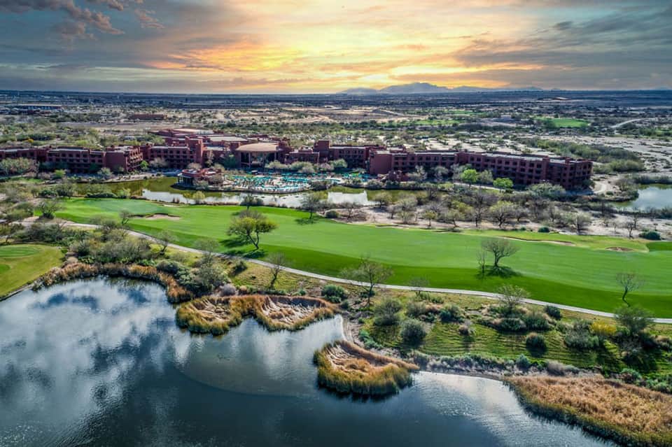 Aerial view of resort property with golf course, ponds, and red brick buildings at sunset.