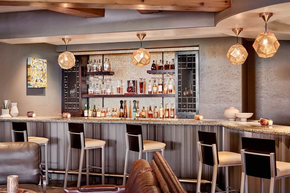 Upscale bar with geometric pendant lights, tiered shelving, and granite countertop