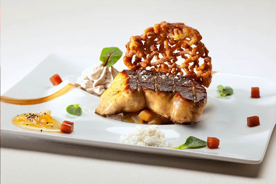 Gourmet plated dish with seared protein, pretzel garnish, and artistic sauce presentation