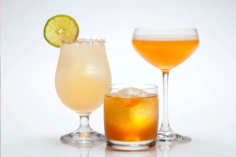 Three cocktails on white background: margarita, whiskey, and tropical drink