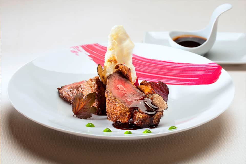 Gourmet plated beef dish with white foam garnish and artistic presentation