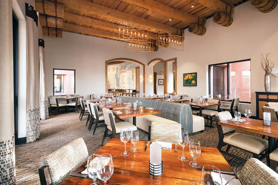 Upscale restaurant with wooden ceiling beams, multiple wooden tables with place settings, and rustic-modern design