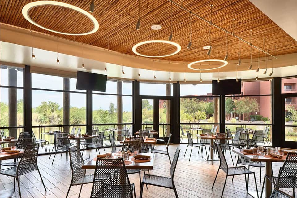Modern restaurant interior with circular ceiling lights, floor-to-ceiling windows, and outdoor views