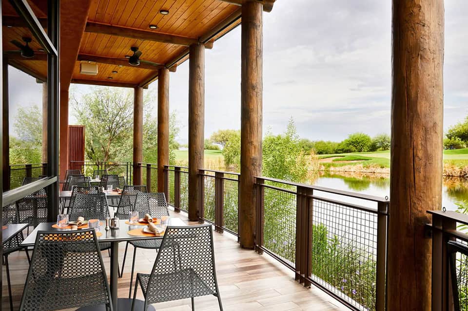 Covered waterfront dining patio with wooden ceiling, black mesh chairs, and river views