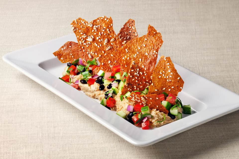Gourmet appetizer plate with crispy sesame crackers and fresh vegetable hummus dip